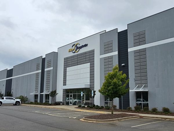Modern industrial building with parking and cloudy sky.