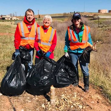 Three volunteers in orange vests holding black trash bags outdoors.
