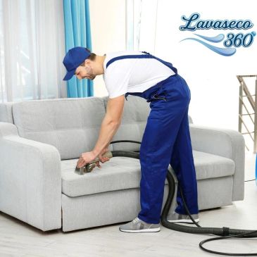 Hombre limpiando un sofá gris con equipo profesional.