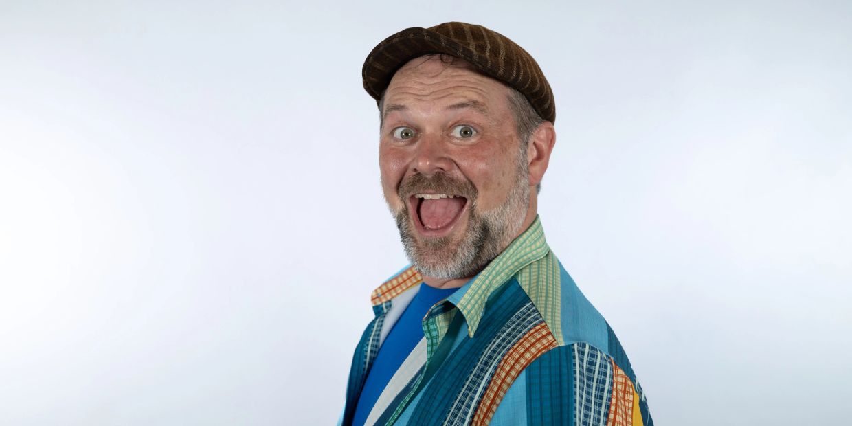 A cheerful man wearing a colorful shirt and brown cap smiling widely.