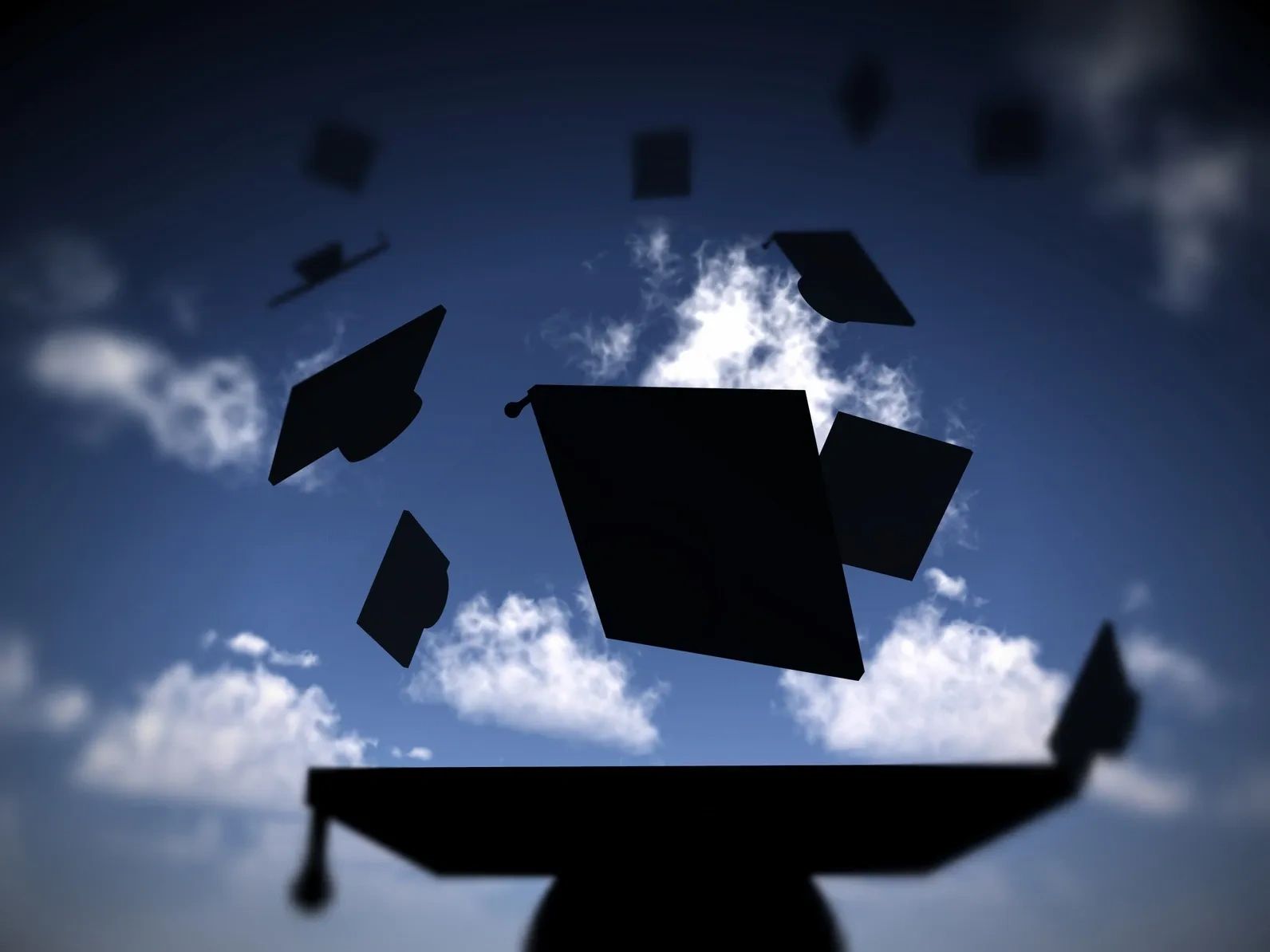 Graduates toss their caps skyward against a blue sky with clouds.