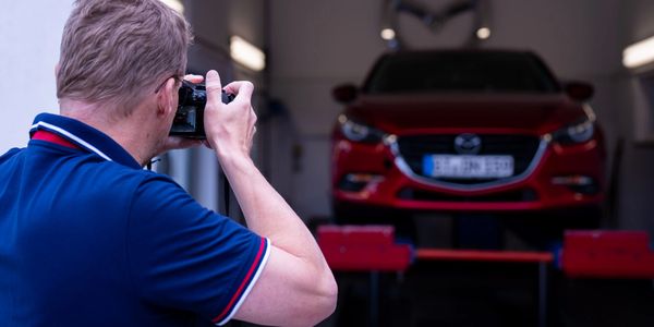 Gutachter fotografiert ein rotes Fahrzeug auf einer Werkstattbühne zur Fahrzeugbewertung