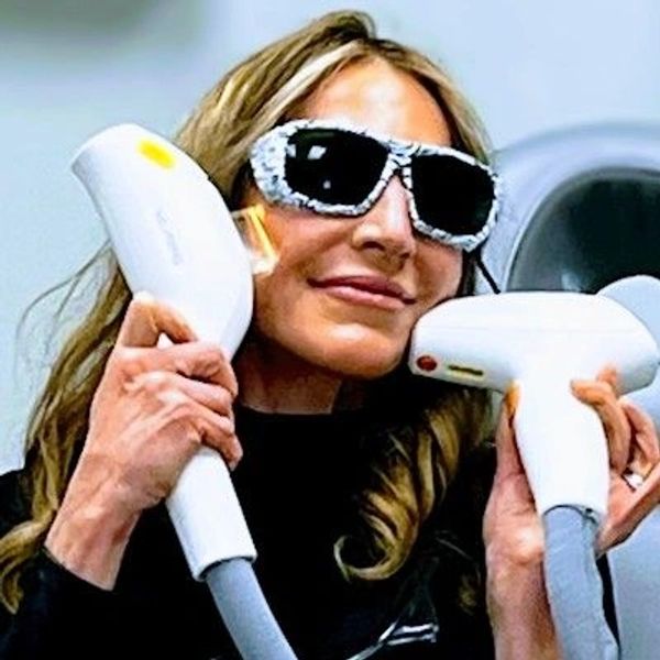 Woman wearing protective glasses holding laser treatment devices near her face.