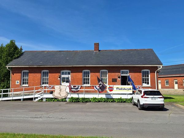 Historic red brick building with flags and a white car parked outside.