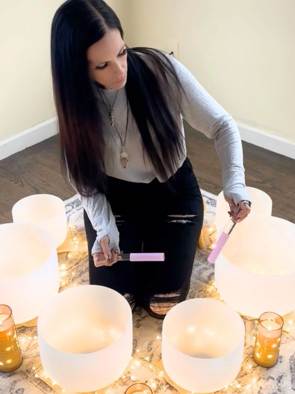 Woman playing crystal singing bowls in a circle with lights.