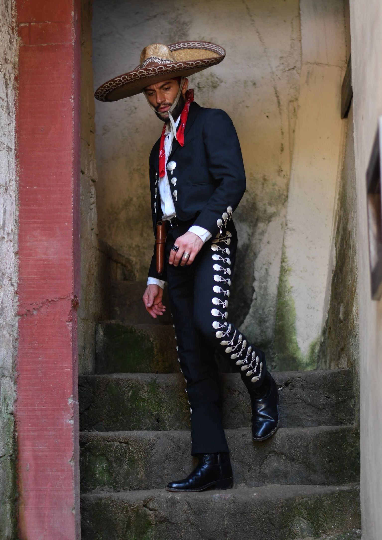 Man in traditional mariachi attire descending mossy stone stairs.