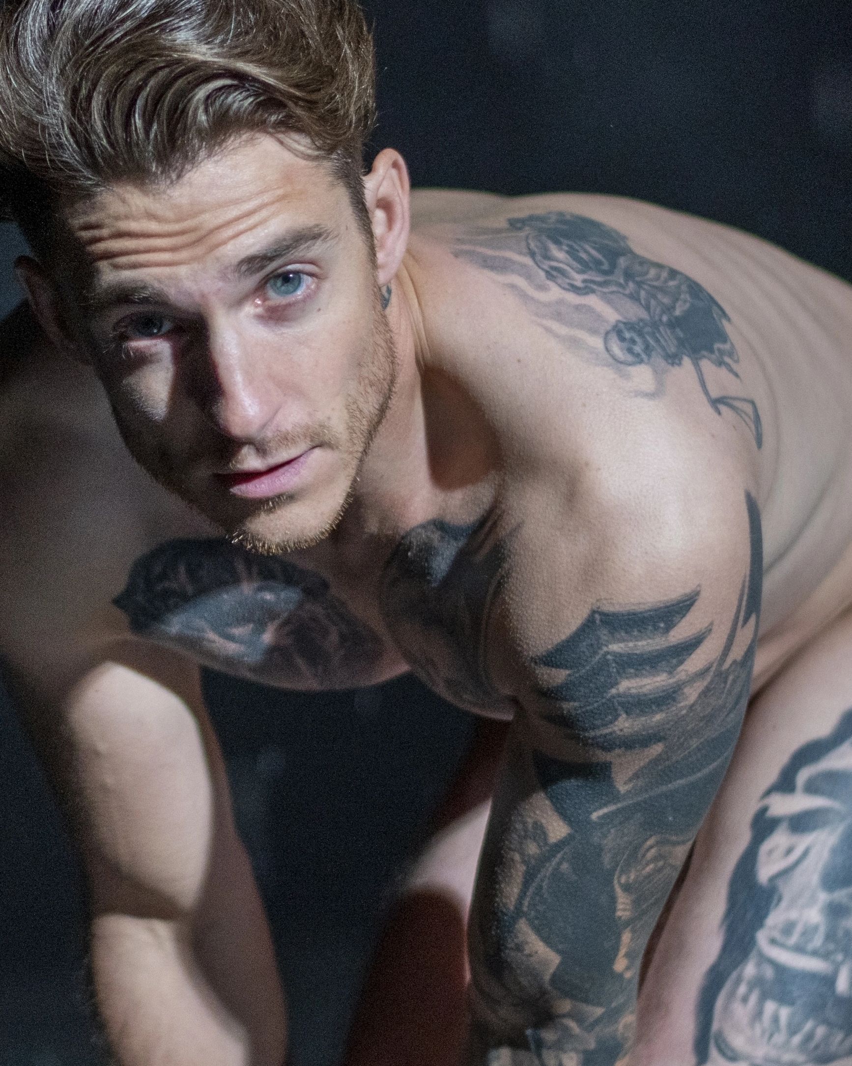 Close-up of a tattooed man with blue eyes looking at the camera.