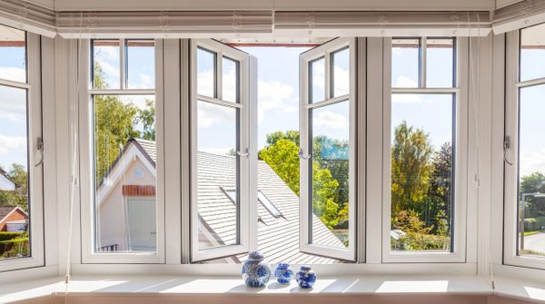 Bright room with white-framed open windows showing a sunny outdoor view.