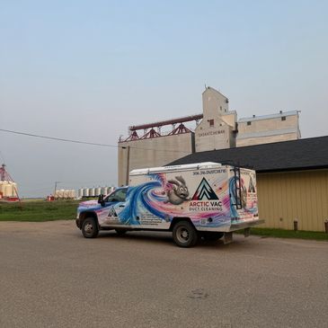 A colorful Arctic Vac truck parked near grain silos.