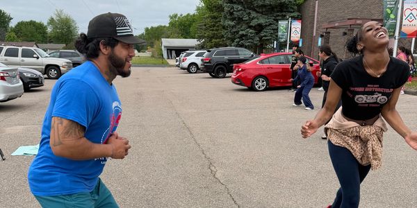 Two people laughing and dancing outdoors in a parking lot.