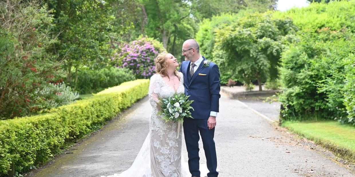 Bride and groom smiling at each other on a garden path.