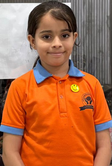 Smiling girl in an orange and blue shirt with a smiley pin.