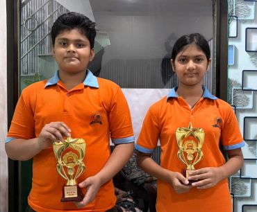 Two children holding "Star of the Month" trophies in orange uniforms.