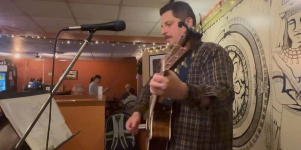 Man playing guitar and singing in a cozy indoor setting.