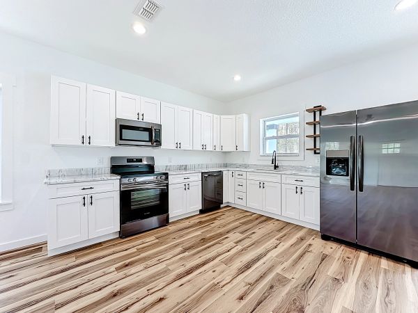 Modern white kitchen with black appliances and wooden floor.