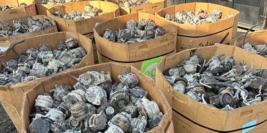 Large bins filled with used automotive alternators and parts in an outdoor scrapyard.