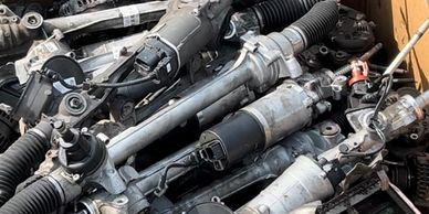 Box filled with various used automotive steering racks and parts.
