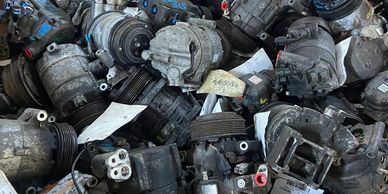 A large pile of used automotive air conditioning compressors in a cardboard box.