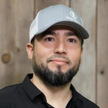A man wearing a gray cap and black shirt with a wooden background.