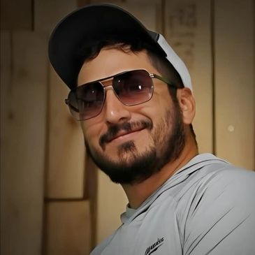 A man wearing sunglasses and a cap smiles warmly at the camera.