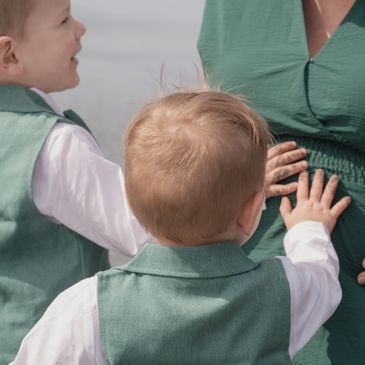 Two young boys touching a pregnant woman's belly, smiling and excited.