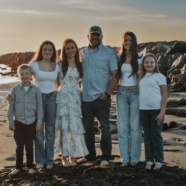 A family of six posing together on a beach during sunset.