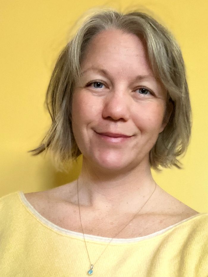 Smiling woman with short blonde hair wearing a yellow top against a yellow background.