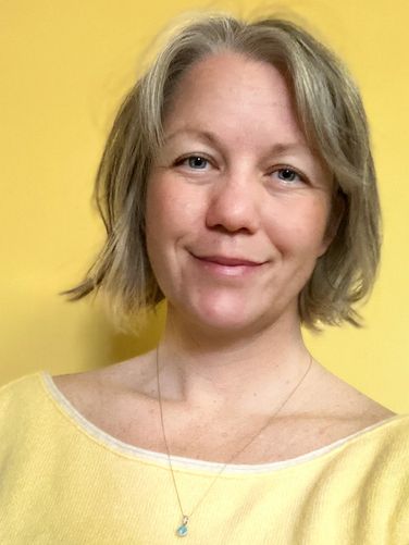 Smiling woman with short blonde hair wearing a yellow top against a yellow background.
