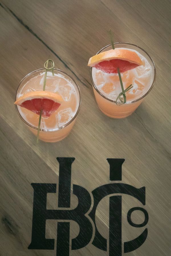 Cocktails with ice and citrus wedges, served on a wooden table with the Urbana Brewing Co. logo.