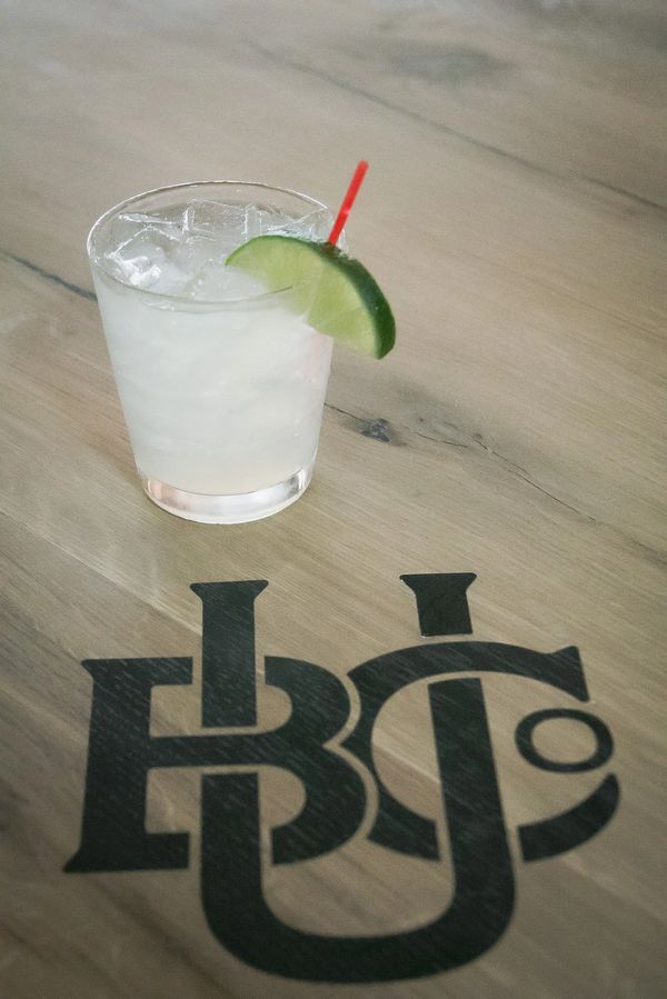Cocktail with lime garnish on table featuring Urbana Brewing Co. logo.