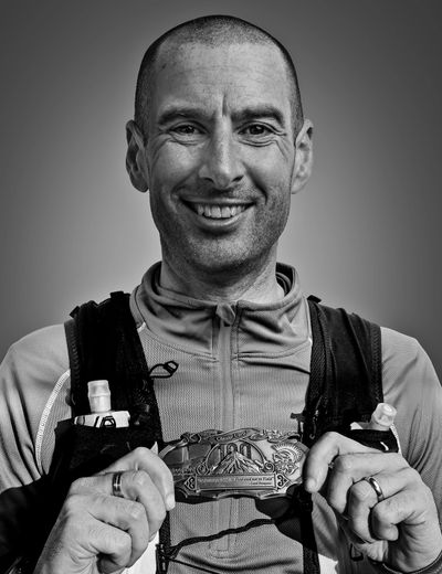Smiling man holding a detailed belt buckle in black and white.