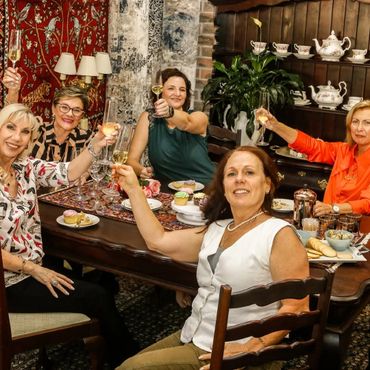 Five women raising glasses in a cheerful toast around a table with food and cupcakes.