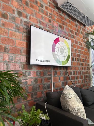 Modern office setup with a TV displaying Enneagram on a brick wall.