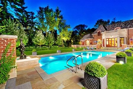 Elegant outdoor pool area with manicured lawn and luxurious house at dusk.