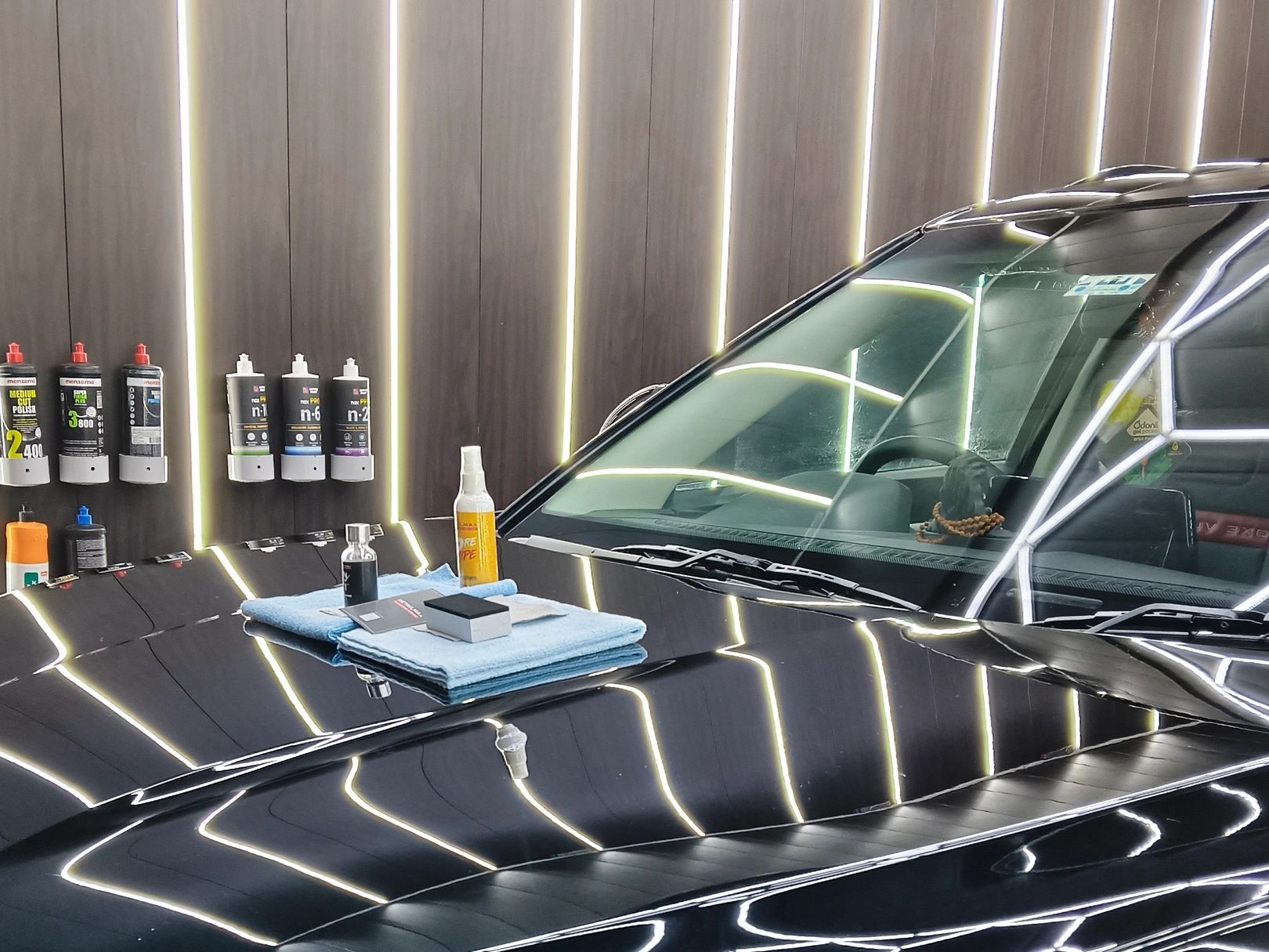 Car detailing products arranged with reflection on a black car hood.