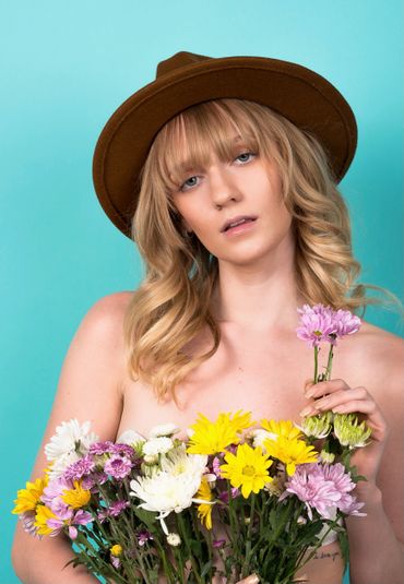 Girl in front of a blue backdrop with meadow flowers and a brown hat on