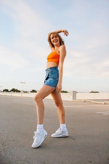 Girl laughing on a rooftop in an orange shirt and jean skirt