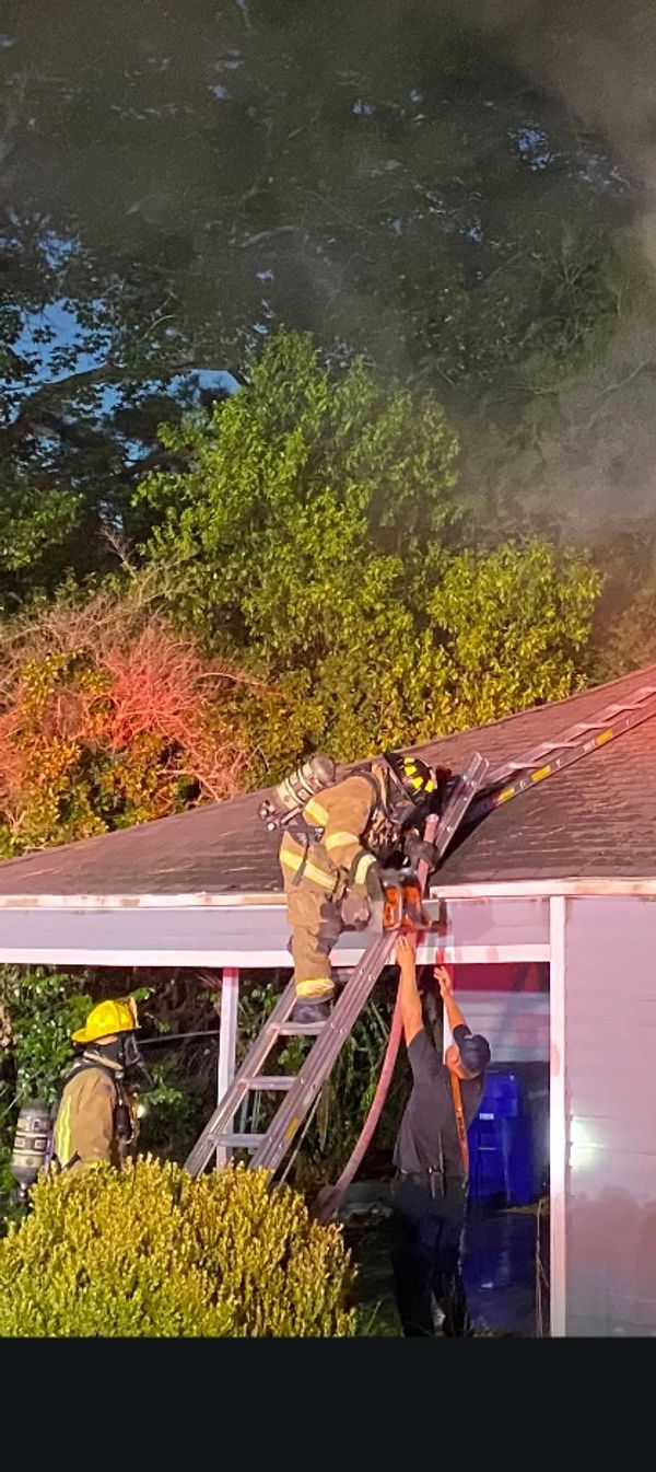 Firefighters in action on a roof with smoke and a ladder.