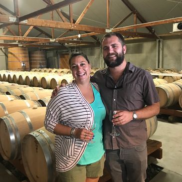 A smiling couple holding wine glasses in a wine barrel cellar.