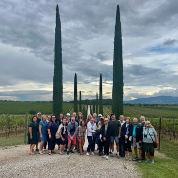 Group of people posing in a vineyard with tall cypress trees and cloudy sky.