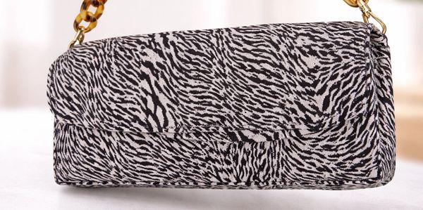 Hand holding a zebra-print handbag with tortoiseshell chain strap.