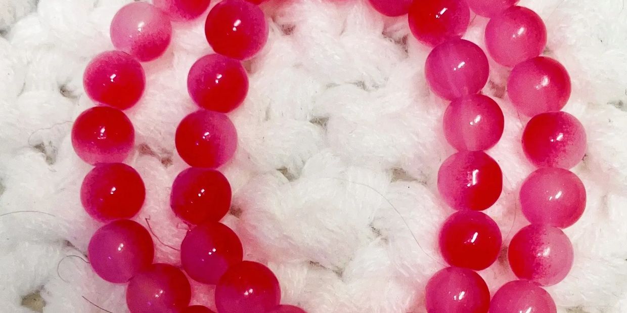 Pink beaded bracelet with a Virgo zodiac charm on a white knitted background.