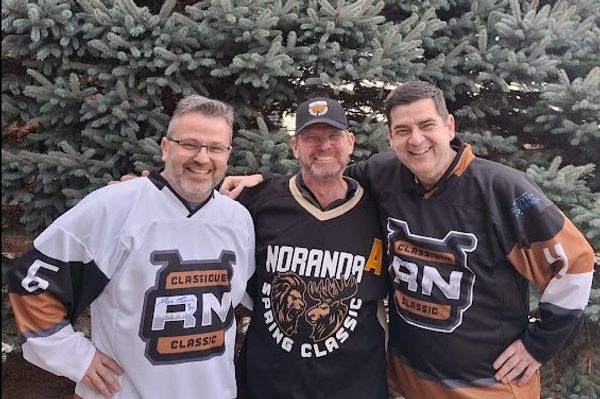 Three men in hockey jerseys smiling outdoors in front of trees.