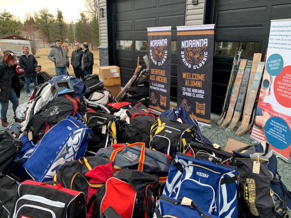 Piles of hockey bags and equipment with Noranda Spring Classic banners in the background.