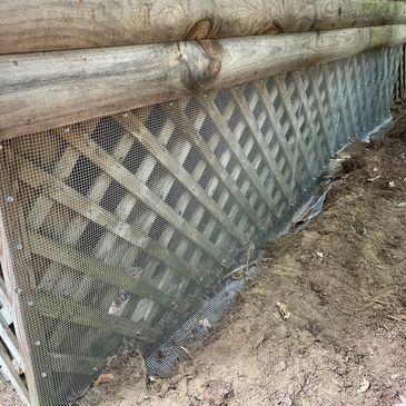 Wood lattice with protective metal mesh installed along a dirt ground.