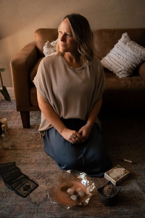 Woman kneeling on floor near a couch with spiritual items.