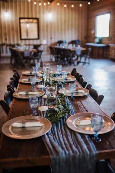 Rustic wooden table set for a formal dinner with elegant blue glassware and greenery.
