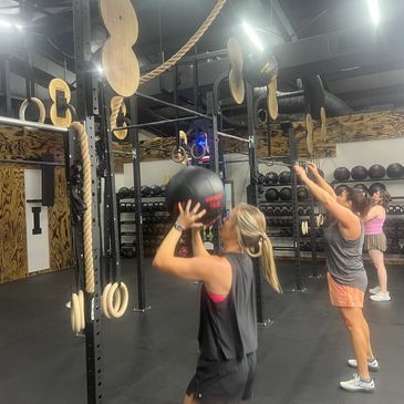 Members doing wall ball exercises in a gym setting.
