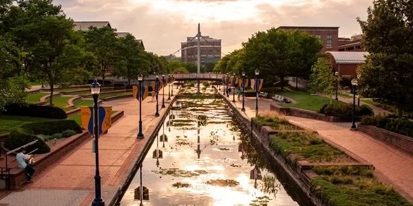 Urban park canal reflecting sunlight with trees and benches along the path.