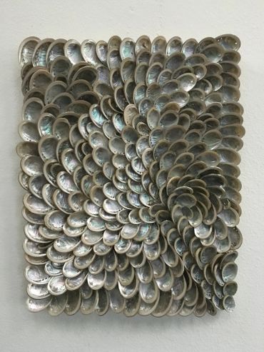 A textured wall art piece made of numerous overlapping shells.
